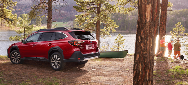 Subaru Outback parked near canoe in front of lake, family with dog looking ahead.